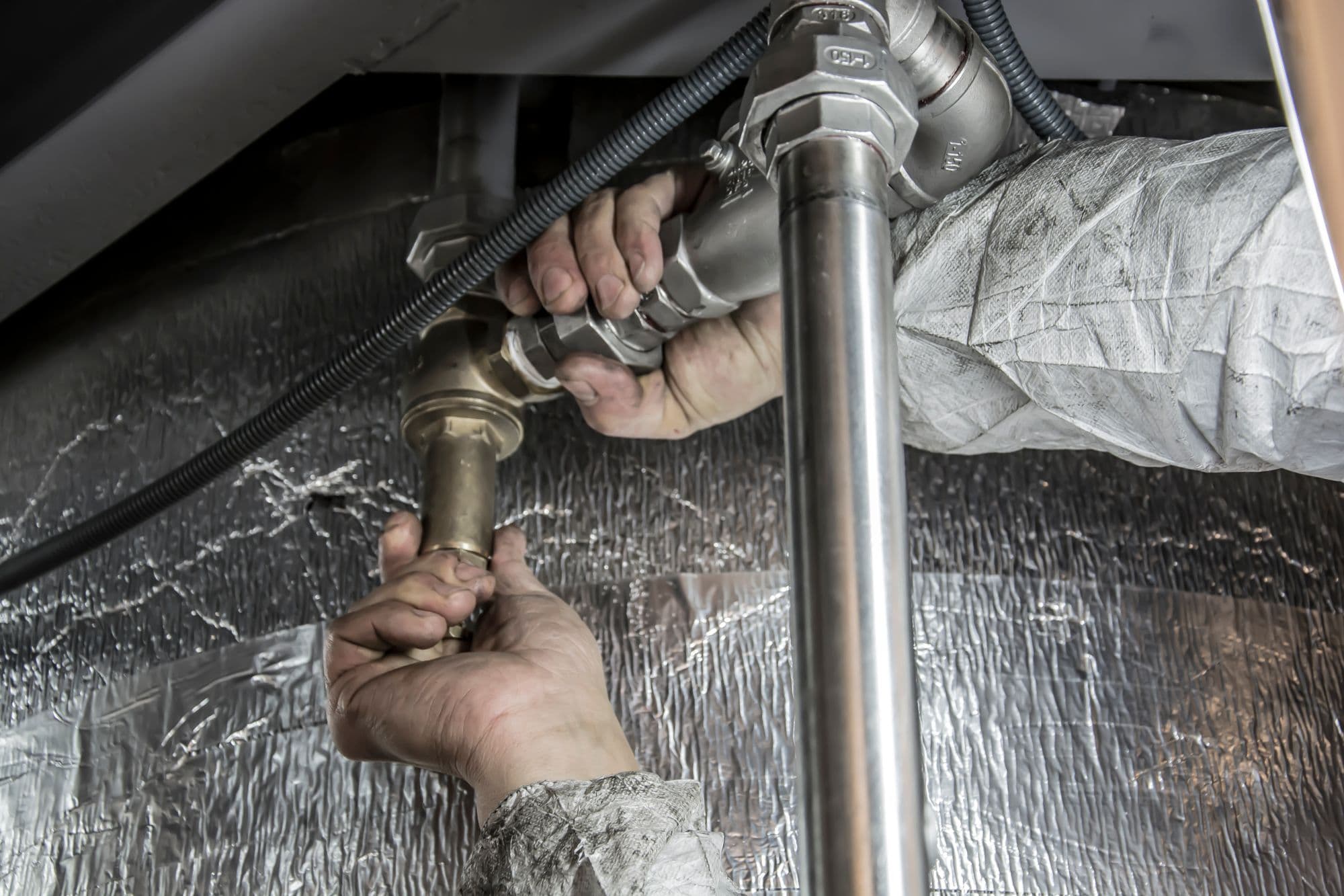 Plumber’s hands working pipe fittings in a residential mechanical room